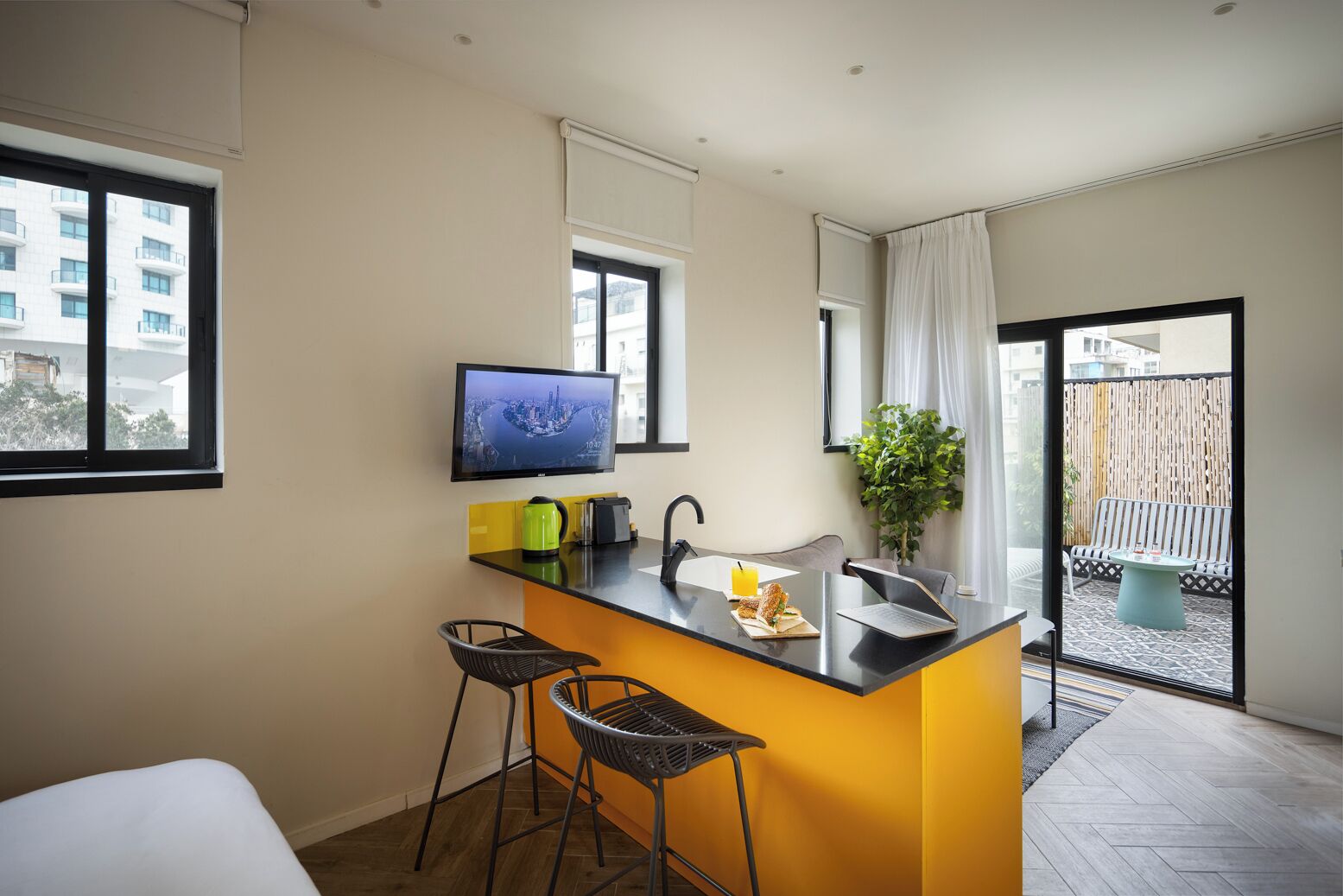 Een moderne keuken met een zwart aanrecht, twee barkrukken, een spoelbak, een waterkoker en een televisie aan de muur.
