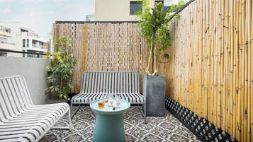Een balkon met twee gestreepte stoelen, een ronde tafel met drankjes en een bamboebeschutting.