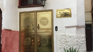 A building entrance with a double golden door, a small window with metal bars, a wall-mounted sign, and a potted plant. - Rent room at Riad Alkatib in the heart of the Medina Meknes (MEKNES)