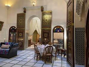 A traditional Moroccan interior with a dining area, ornate doors, and a sofa. - Rooms for Rent at Riad Alkatib in the Heart of the Meknes Medina (MEKNES)
