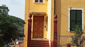 Un bâtiment à deux étages, doté d’une façade jaune, d’une porte en bois et d’un petit porche avec des marches menant à l’entrée.