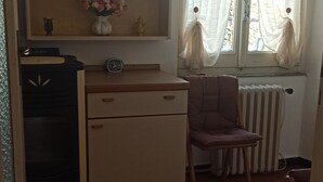 Une petite cuisine équipée d’un réfrigérateur, d’une chaise et d’une fenêtre avec des rideaux.