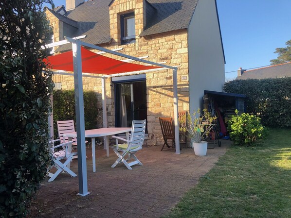An outdoor patio with a table and chairs, a red canopy, and a stone building in the background.