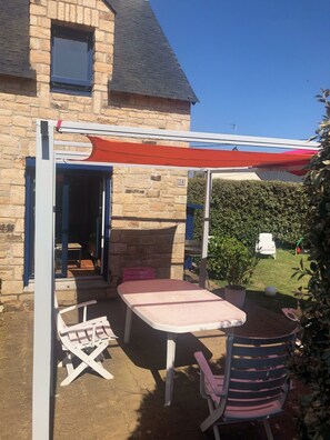 Una casa in pietra con un patio attrezzato con tavolo e due sedie, un’area salotto coperta e un siepe sullo sfondo.