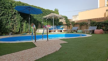 Un jardin avec une piscine, un parasol, un coin salon avec une table et des chaises, et une petite terrasse.