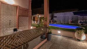 A poolside area with a lounge chair, potted plants, and a well-lit outdoor space.