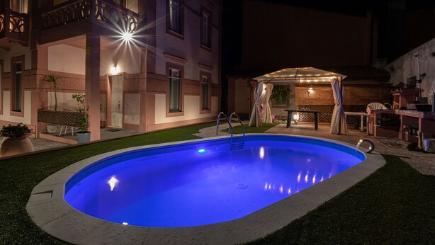 A swimming pool with a blue light, a covered patio, and a building with balconies.