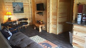 Un accogliente interno di una baita con un divano, poltrone, un tavolino e un televisore montato a parete.
