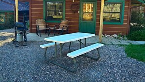 A rustic cabin with a covered patio, picnic table, and outdoor seating.