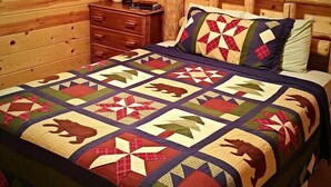 A wooden cabin bedroom with a large bed, a nightstand, a mirror, and a quilt with animal patterns.
