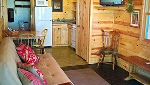 A cozy cabin interior with a wooden interior, a sofa, a dining table, a kitchen area, and a ceiling fan.