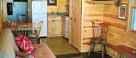 A cozy cabin interior with a wooden interior, a sofa, a dining table, a kitchen area, and a ceiling fan.