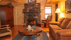 A cozy log cabin interior with a stone fireplace, wooden furniture, and a framed picture on the wall.