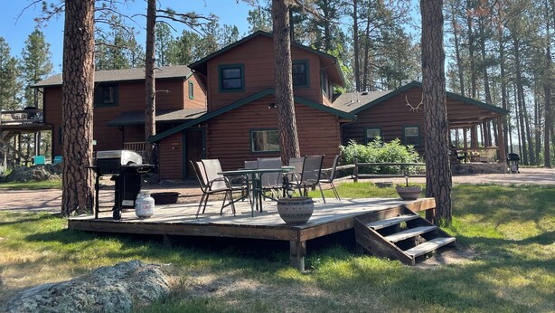 A cabin with a deck, outdoor seating, and a grill area.