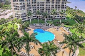 A hotel with a large pool surrounded by palm trees and lounge chairs. - Beachfront Condo | Views, Pool & Tennis Courts (Marco Island)