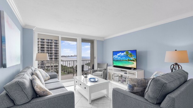 A modern living room with grey sofas, a white coffee table, and a TV on a stand. - Beachfront Condo | Views, Pool & Tennis Courts (Marco Island)