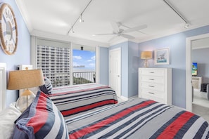 A bedroom with a large bed, a ceiling fan, a window with a view, a dresser, and a lamp. - Beachfront Condo | Views, Pool & Tennis Courts (Marco Island)