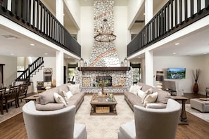 A spacious living area with a stone fireplace, a large sofa set, and a staircase connecting two floors.