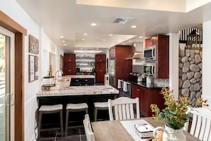 A modern kitchen with a central island, bar stools, and a dining table with chairs. - Ski Lodge 2 Min to Slopes · Sleeps 16 · Game Room (Big Bear)