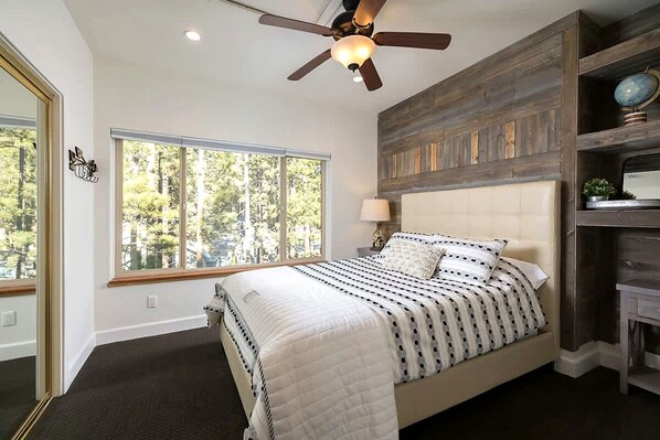A bedroom with a bed, a ceiling fan, a window, and a wooden wall panel.