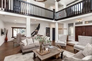 A spacious living area with a high ceiling, a staircase, and a view of the outdoors.