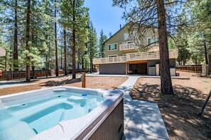A two-story house with a hot tub in the backyard, surrounded by tall pine trees. - Ski Lodge 2 Min to Slopes · Sleeps 16 · Game Room (Big Bear)