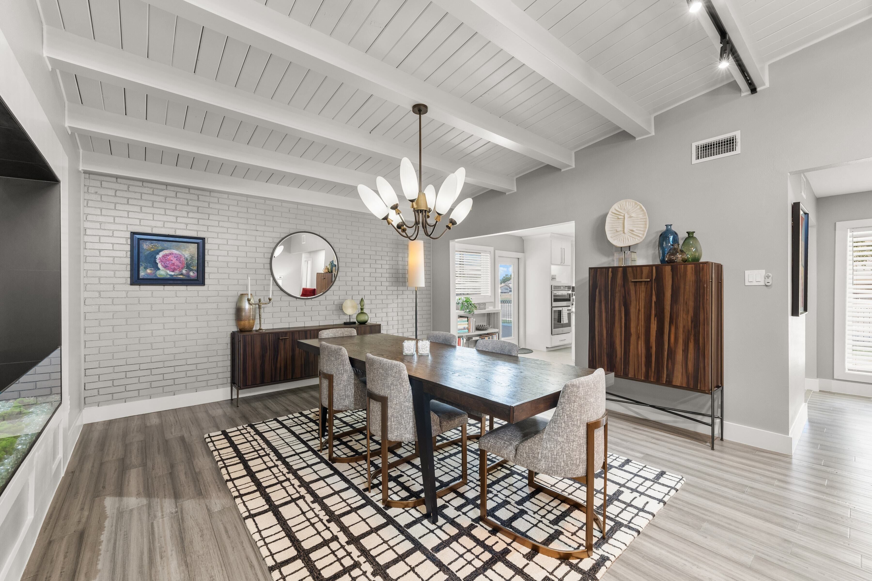 A modern kitchen with white brick walls, a wooden dining table, and a patterned rug.