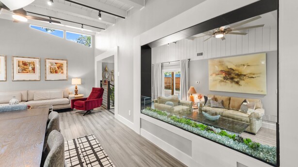 A spacious living room with a glass coffee table, a red chair, and a large window overlooking a garden. - Preston Hollow Retreat (Dallas)