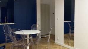 Een moderne keuken met donkerblauwe kastjes, een witte eettafel met transparante stoelen, en een grote spiegel die de ruimte weerspiegelt.