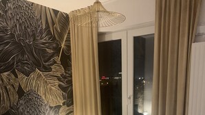Een slaapkamer met een bedovertrek met dessin, een bedlampje en uitzicht op de stad 's nachts door een raam met gordijnen.