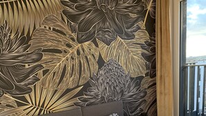 Een slaapkamer met een bed met een patroon, een groot raam met uitzicht en een wand met een bloemendesign.