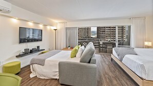 A hotel room with two beds, a sofa, a TV, and a balcony with a city view.