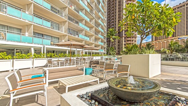 A rooftop lounge with outdoor seating, a fire feature, and a view of a high-rise building.