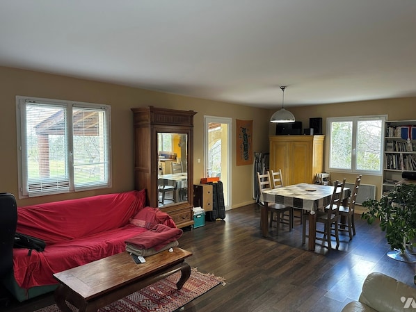 A living room with a red sofa, wooden coffee table, dining table with chairs, and a bookshelf.