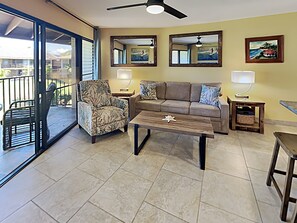 A living room with a sofa, armchair, coffee table, and two side tables with lamps. There are two wall-mounted mirrors and a ceiling fan. - Stunning Kihei Condo New Split AC Ocean and Pool Views Large Lanai Beach (Kihei)