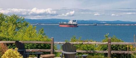 Een terras met buitenmeubilair, uitzicht op zee en een schip in de verte.