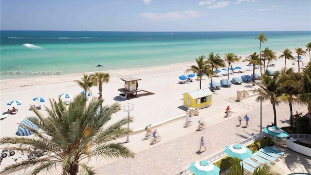 A beach with a row of palm trees, beach umbrellas, and a lifeguard tower. - Beach Front Spacious 1BR , The Tides, Hollywood,FL (Hollywood)