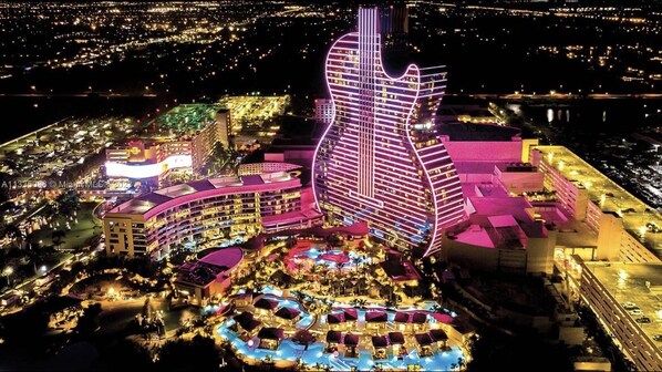 Un hotel con un edificio con forma de guitarra, varias piscinas y una zona de resort bien iluminada.