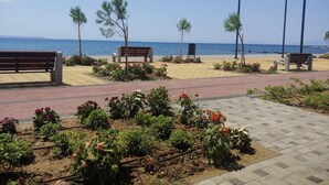 Une promenade dallée, agrémentée de bancs et de lampadaires, qui mène à une plage avec la mer en toile de fond.