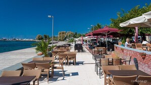 Un café en plein air, avec des meubles en osier et des parasols, donnant sur une étendue d’eau.