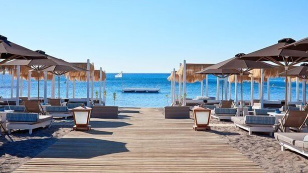 Une promenade en bord de mer qui mène à des chaises de plage et des parasols, offrant une vue dégagée sur la mer.