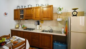 A kitchen with wooden cabinets, a gas stove, a sink, and a refrigerator. - Casa Marta (Nuoro)
