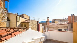 A rooftop terrace with a stone wall, a tiled roof, and a view of the surrounding buildings. - Casa Marta (Nuoro)