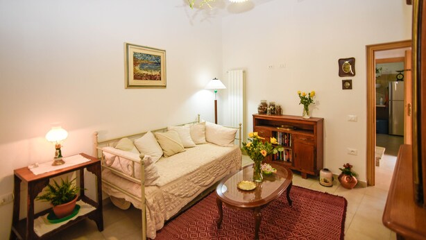 A cozy living room with a sofa, a small table with a lamp, a bookshelf, and a potted plant. - Casa Marta (Nuoro)