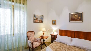A hotel room with a bed, a chair, a table with a lamp, and two framed pictures on the wall. - Casa Marta (Nuoro)