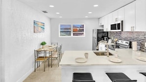 A modern kitchen with white cabinets, a central island, and a dining area with a table and chairs.