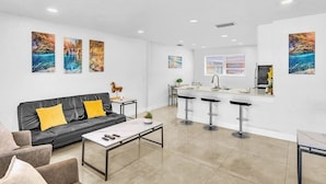 A modern living room with a black leather sofa, a coffee table, and a kitchen area with a bar stool seating.