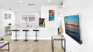 A modern kitchen with a central island, bar stools, and a large flat-screen TV mounted on the wall.