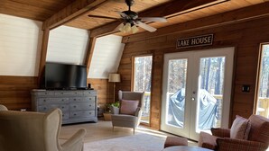 L’intérieur d’un chalet accueillant, avec une télévision posée sur une commode, une cheminée et une pancarte indiquant « MAISON AU BORD DU LAC ».