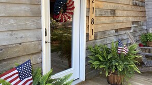 Une maison en bois avec une porte blanche, une guirlande ornée d’un drapeau américain et le numéro « 2181 » peint sur le mur.